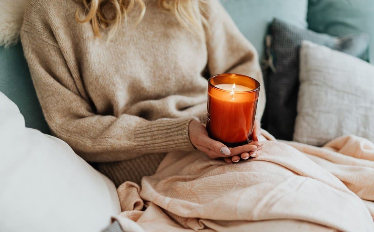 Woman holding a lit amber candle, taking a quiet moment at home
