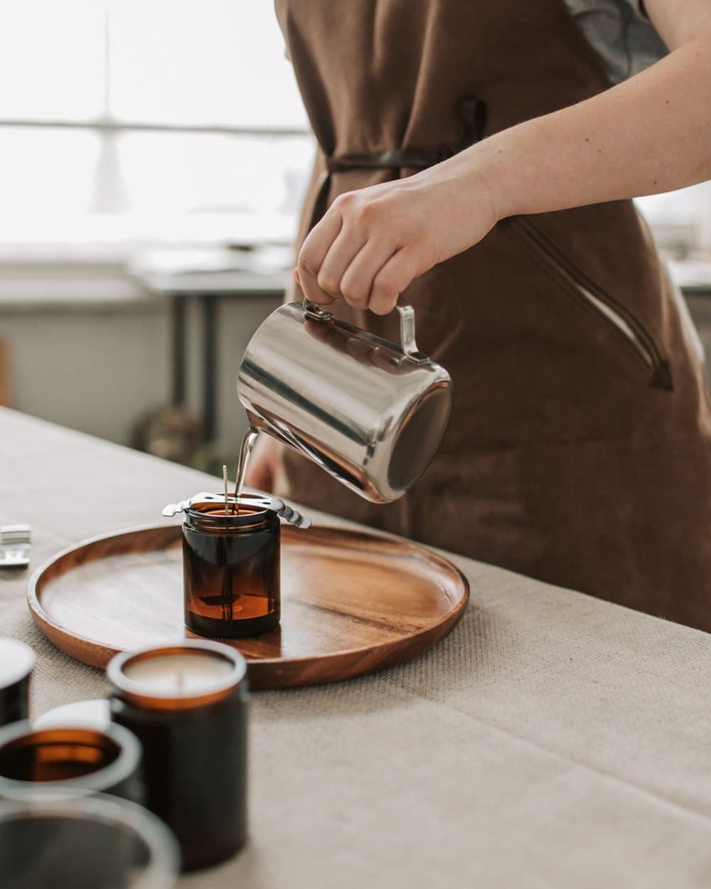 Store owner pouring soy wax into amber candle jars in her workshop